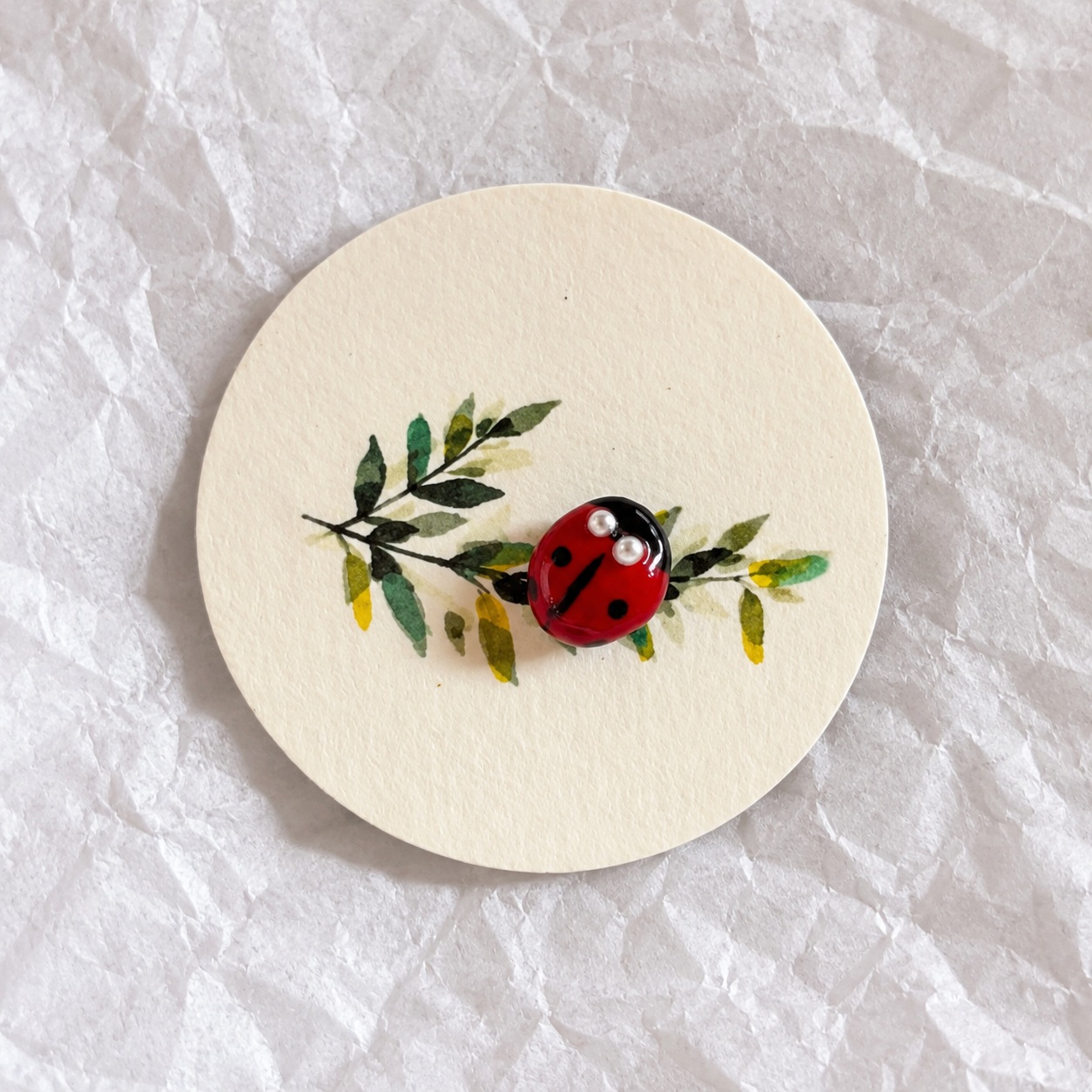 Détail d’un pin’s coccinelle rouge et noir, avec deux petites perles pour les yeux