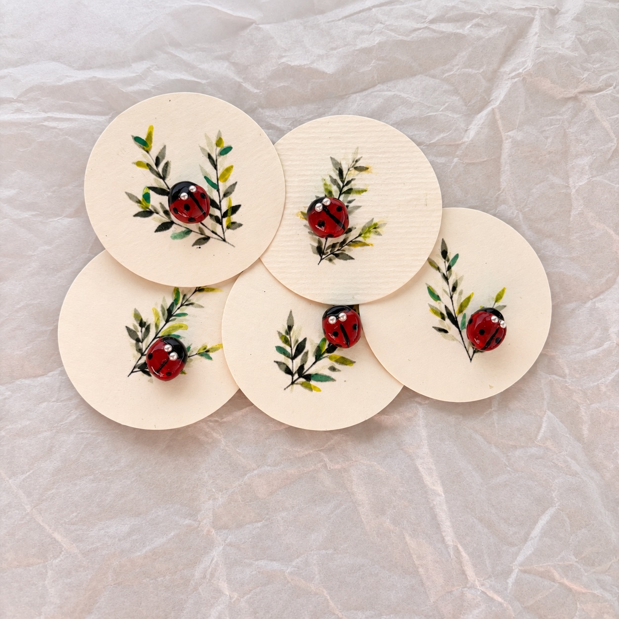Cinq pin’s coccinelles sur leurs cartes rondes illustrées de branches
